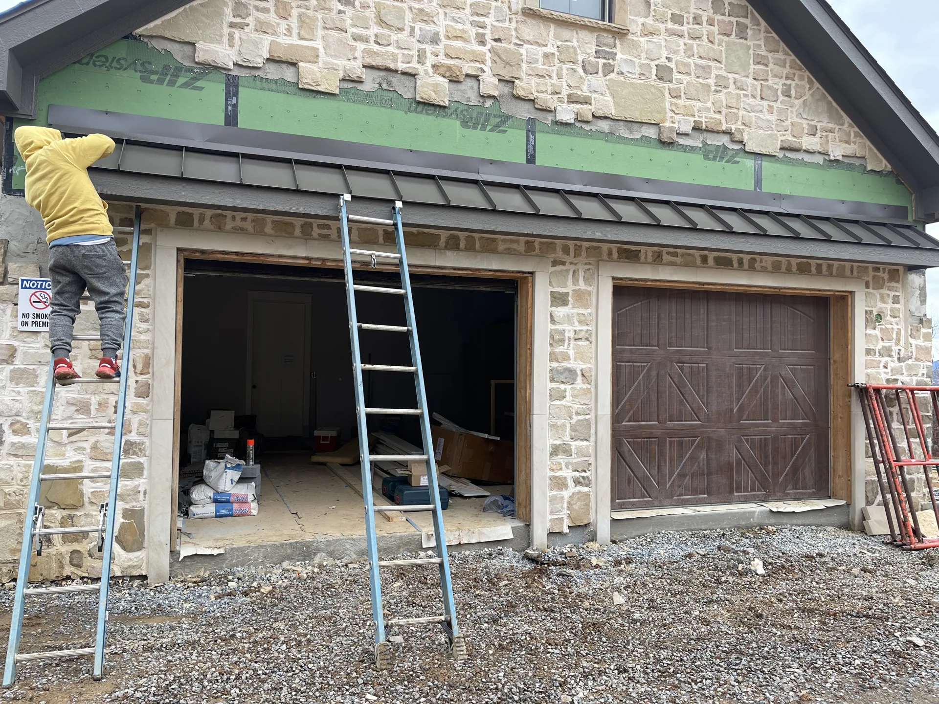 Workers installing metal roofing above a stone-clad entry